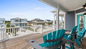 Une terrasse en bois, avec des chaises turquoise et une table, donnant sur une rangée de maisons.