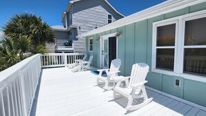 Une maison située sur la côte, dotée d’un porche, de chaises berçantes blanches et offrant une vue sur l’océan.