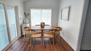 Un coin repas avec une table et des chaises en bois, un vase orné de branches et une fenêtre avec des stores.