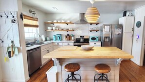 Une cuisine compacte dotée d’un îlot central, de tabourets en bois, d’un four encastré, d’un four à micro-ondes et d’un réfrigérateur.