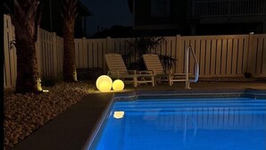 Une piscine entourée d’une terrasse en bois, de chaises longues et d’une clôture blanche.