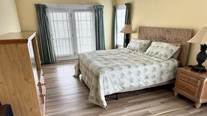 Ein Schlafzimmer mit einem Bett, Nachttischen aus Holz, einer Kommode und einem Fenster mit Vorhängen.