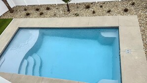 Ein rechteckiger Swimmingpool mit einer befliessten Kante, umgeben von Kiesbett und weißem Zaun.