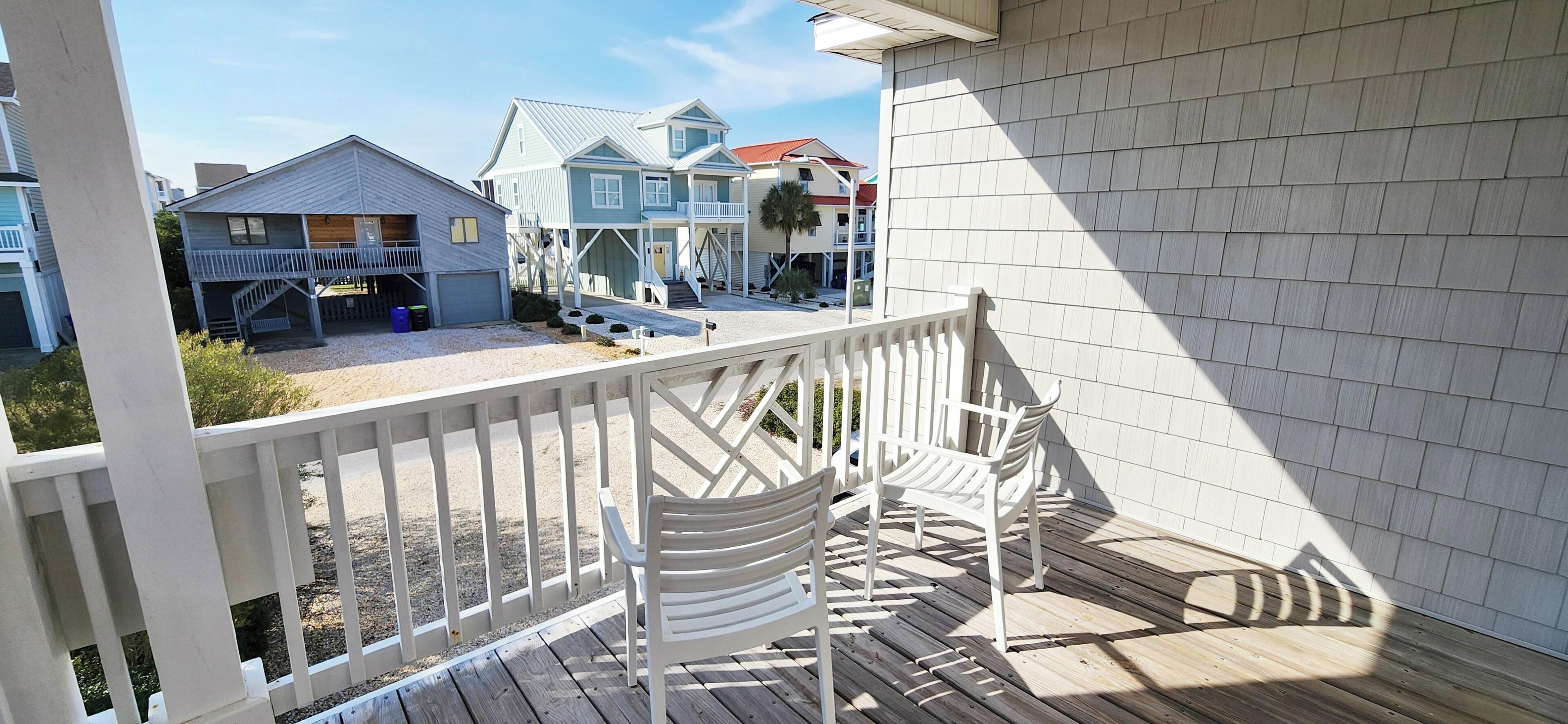 A wooden deck with white railings, a covered area with benches, and a view of neighboring houses.