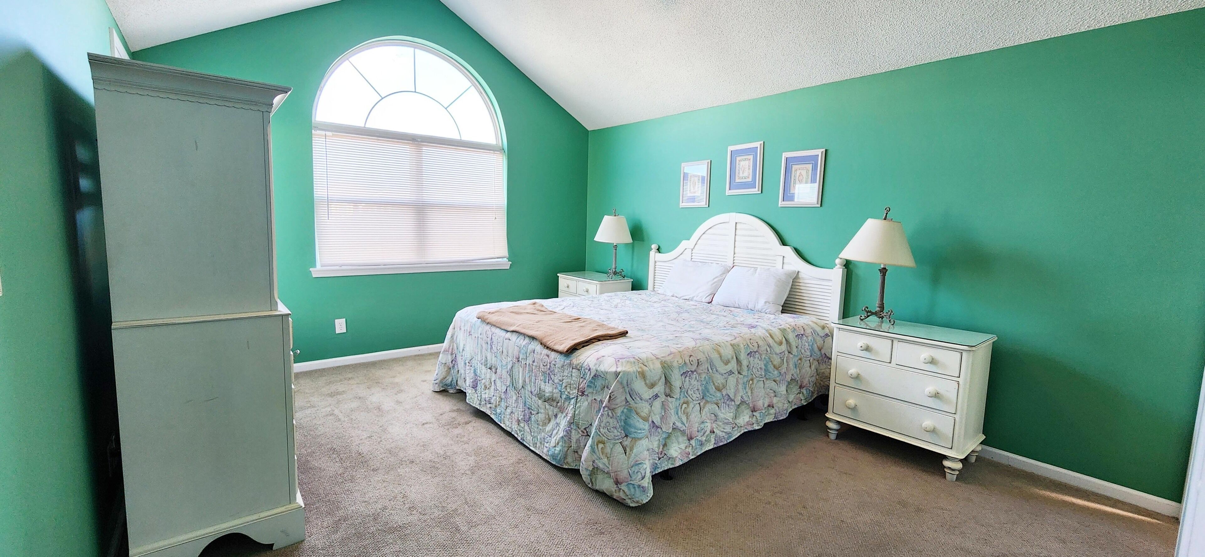A bedroom with a large bed, a dresser, and a window with blinds.