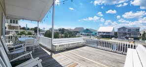 Eine Holzterrasse mit weißen Geländern und Bänken, mit Blick auf ein Wohngebiet mit Häusern und blauem Himmel.