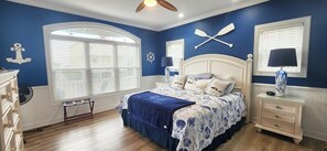 Un dormitorio con cama, mesita de noche, cómoda, ventana con persianas y ventilador de techo.