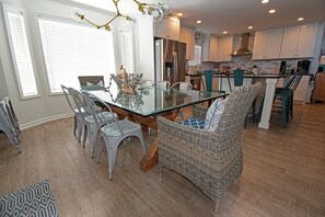 A modern kitchen with white cabinets, a glass dining table, and wicker chairs. - Large 6 bedroom oceanfront beach house (Ocean Isle Beach)