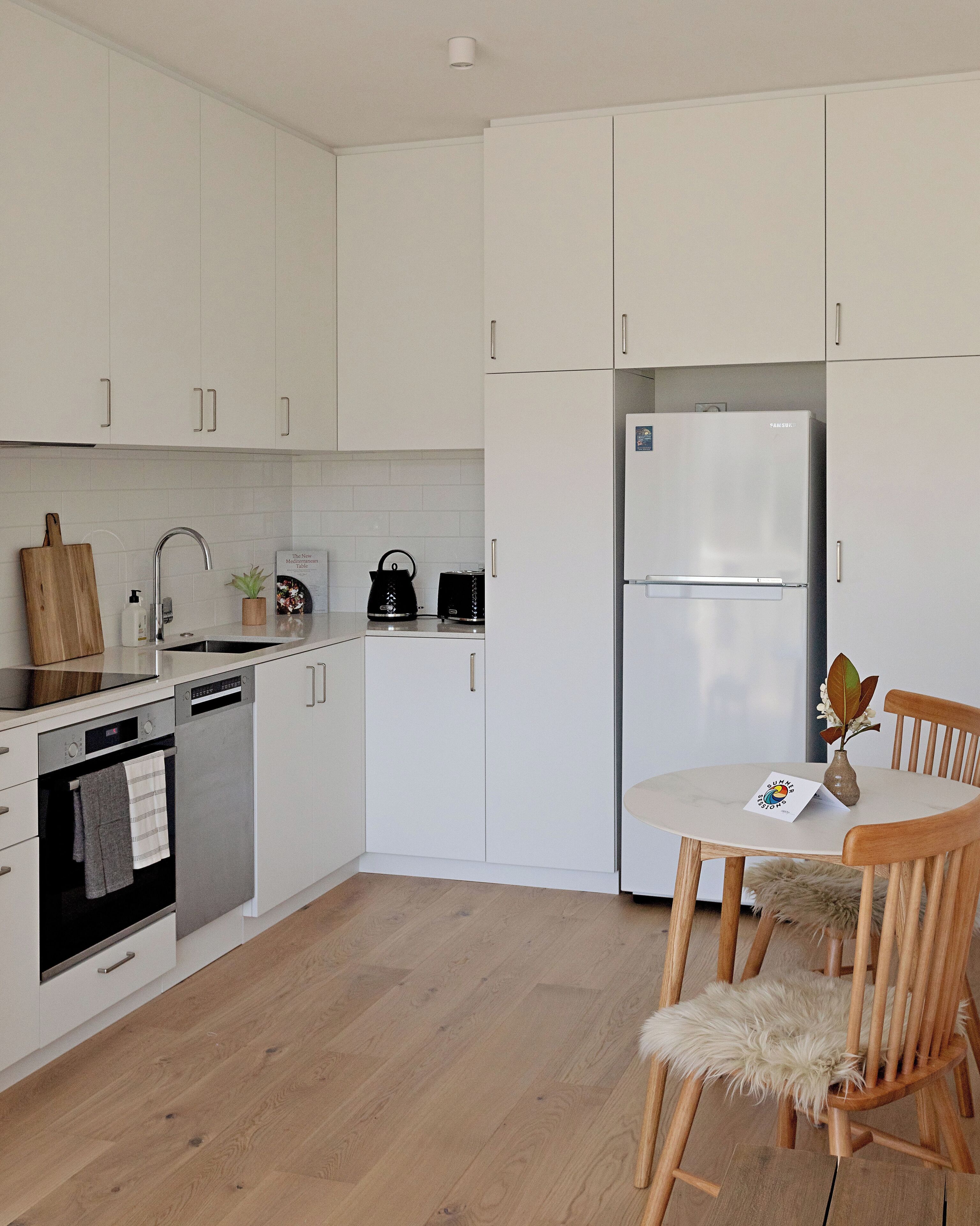 Eine moderne Küche mit weißen Schränken, einem Edelstahl-Kühlschrank, einer Spülmaschine und einem Holzespeisetisch mit Stühlen.