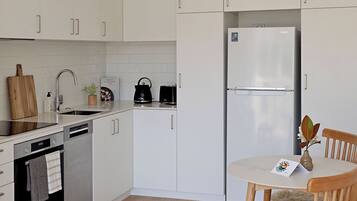 Eine moderne Küche mit weißen Schränken, einem Edelstahl-Kühlschrank, einer Spülmaschine und einem Holzespeisetisch mit Stühlen.