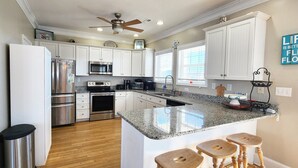 A modern kitchen with white cabinets, stainless steel appliances, a granite countertop, and a ceiling fan. - 5 bedroom house with pool, close to center of town (Ocean Isle Beach)