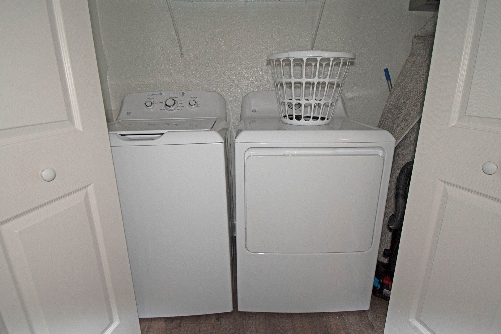 A laundry room with two white washing machines and a white laundry basket on top of the larger machine.
