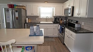 Una cocina compacta con armarios blancos, un refrigerador de acero inoxidable, un microondas y un lavamanos.