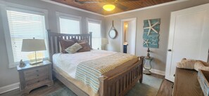 A bedroom with a wooden bed, a nightstand, a lamp, a wall clock, and a starfish decoration. - Cute 3 bedroom oceanfront cottage, sleeps 6 (Ocean Isle Beach)