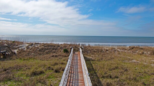 Eine Holzpromenade führt zu einem Strand mit freiem Blick auf das Meer.