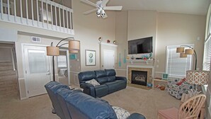 Ein Wohnzimmer mit Sofa, Sessel, Kamin, Fernseher und Deckenventilator.
