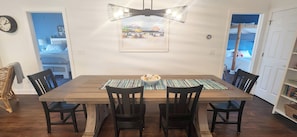 A dining area with a wooden table, black chairs, a woven placemat, and a ceiling light fixture. - New 3 bedroom house private pool, close to beach (Ocean Isle Beach)