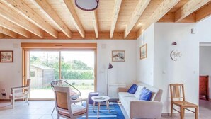 Un salon spacieux doté d’un plafond en bois, d’une grande porte-fenêtre coulissante donnant sur un jardin et d’un canapé agrémenté d’un tapis à rayures bleues et blanches.