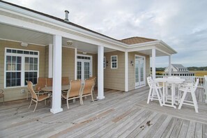 A covered outdoor deck with wooden furniture and white railings. - Shore Beats Work 5 BR/5BA Private Pool, Closet to Beach (Ocean Isle Beach)