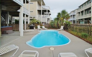 A swimming pool with lounge chairs, surrounded by a wooden fence and palm trees. - Shore Beats Work 5 BR/5BA Private Pool, Closet to Beach (Ocean Isle Beach)
