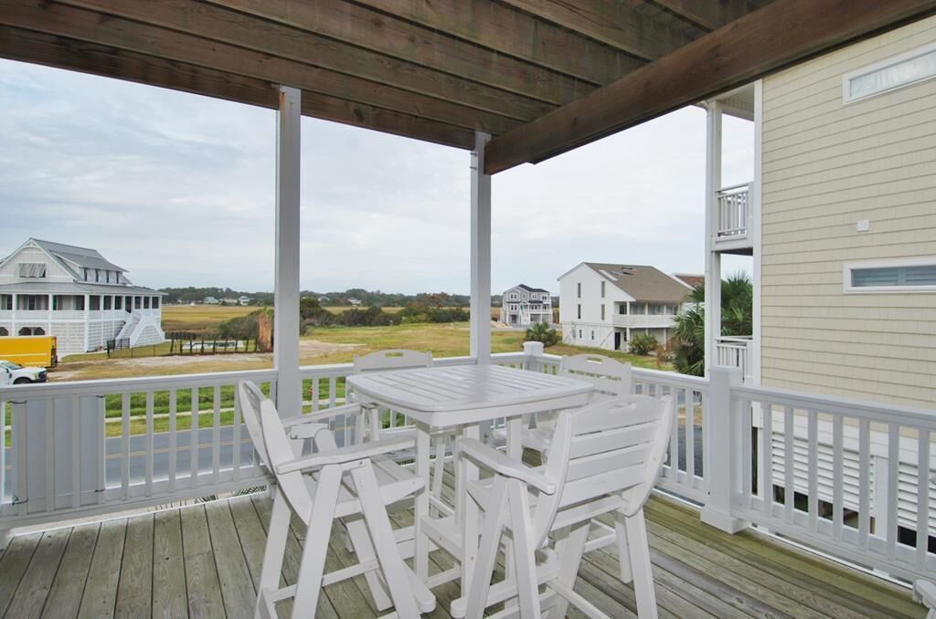 A covered outdoor area with a wooden deck, white furniture, and a view of houses and open land.