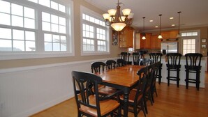 Un comedor amplio con una gran mesa de madera y sillas negras, rodeado de ventanas grandes y un candelabro.