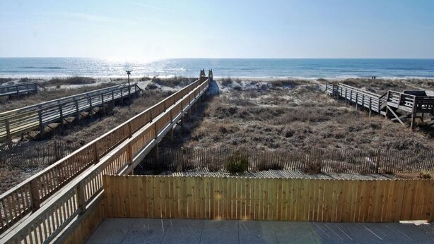 Een houten vlonder die naar het strand leidt, met een helder uitzicht op de oceaan.
