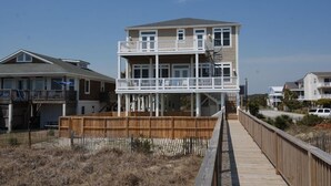 Een twee verdiepingen tellend strandhuis met een balkon, een houten terras en een helder uitzicht op het strand.