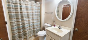 A bathroom with a striped shower curtain, a toilet, a sink with a mirror, and a towel rack. - Stones Throw 4 BR Ocean View Beach House (Ocean Isle Beach)