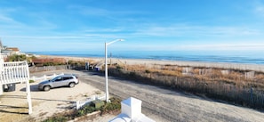 A coastal road with a parked car, a white fence, and a beach in the background. - Stones Throw 4 BR Ocean View Beach House (Ocean Isle Beach)
