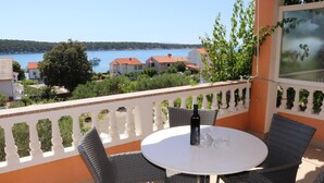 A balcony with wicker chairs and a table, overlooking a body of water and buildings. - A2 comfortable apartment with terrace, garden and sea view (Barbat na Rabu)