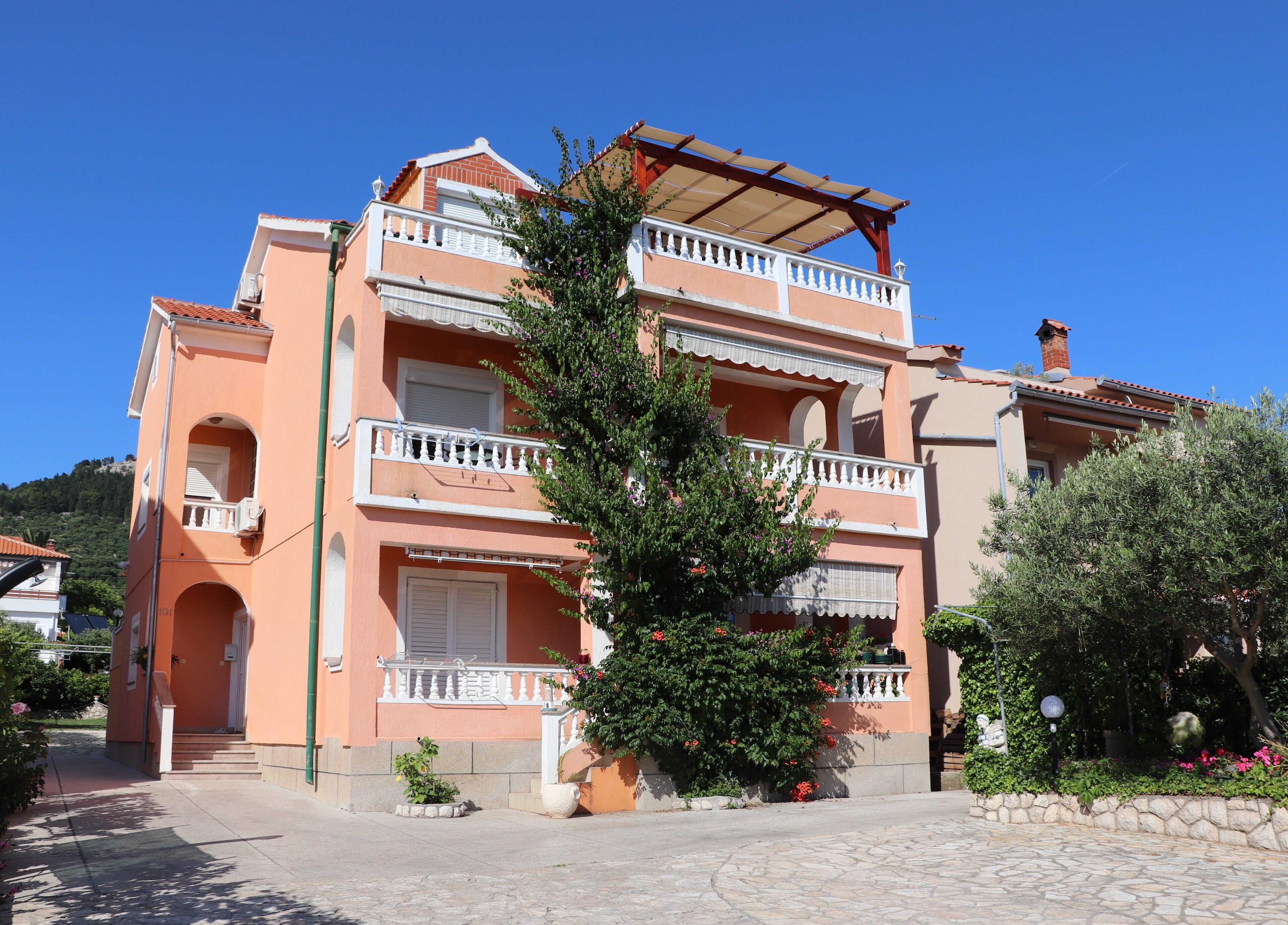 Un immeuble à plusieurs étages doté de balcons, d’un patio couvert et d’un chemin en pierre menant à l’entrée.