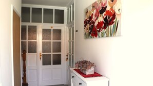 A hallway with a white door, a small white cabinet with a red cloth, and a floral painting on the wall. - A2 comfortable apartment with terrace, garden and sea view (Barbat na Rabu)