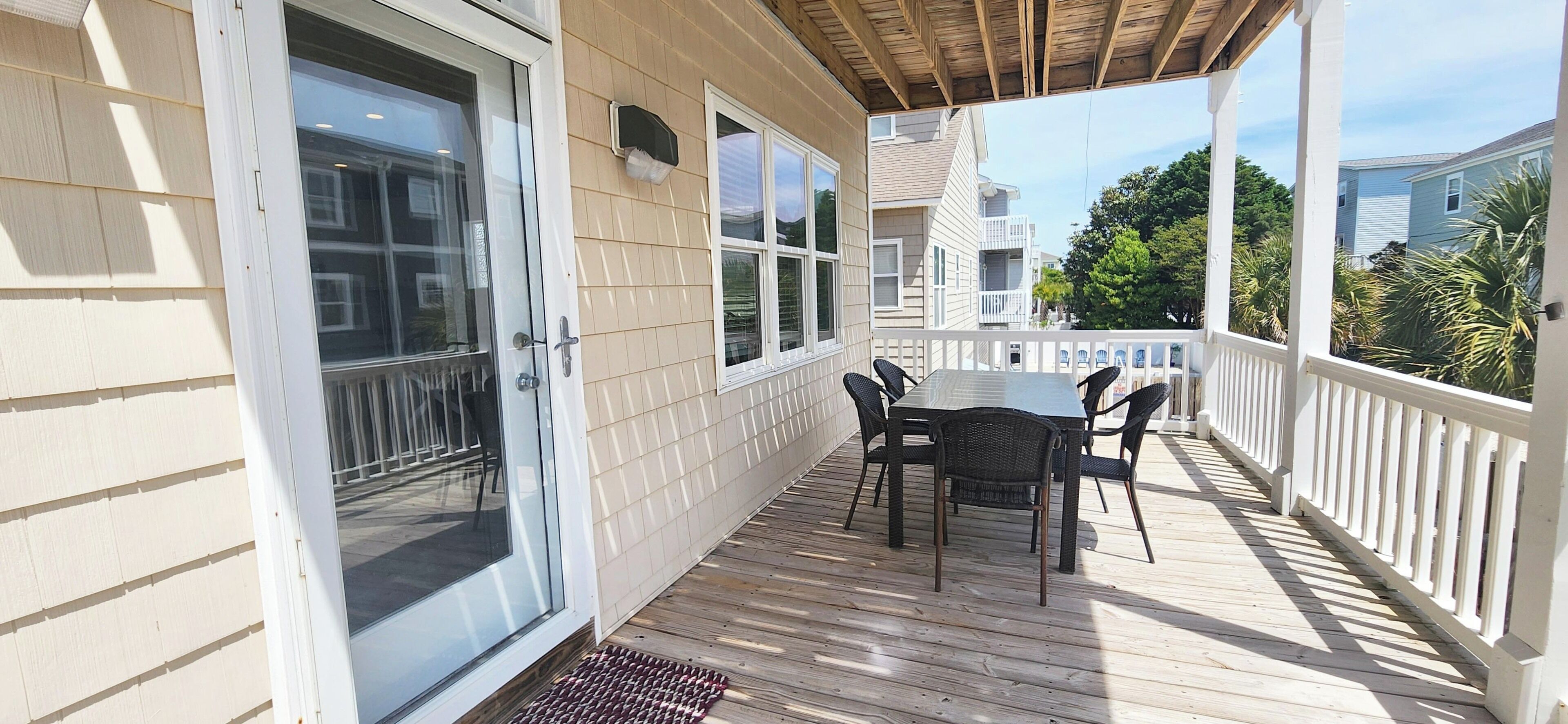 Une terrasse couverte avec une table et des chaises, une porte-fenêtre coulissante et une clôture blanche.