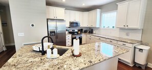 A modern kitchen with white cabinets, stainless steel appliances, granite countertops, and a built-in oven. - A Southern Escape 5 BR Summer Place Home (Ocean Isle Beach)