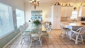 Un espace repas avec une table en verre, des chaises blanches et un lustre.