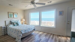Une chambre à coucher avec un lit, un ventilateur de plafond, une table de chevet, une lampe, un téléviseur et une vue sur l’océan.