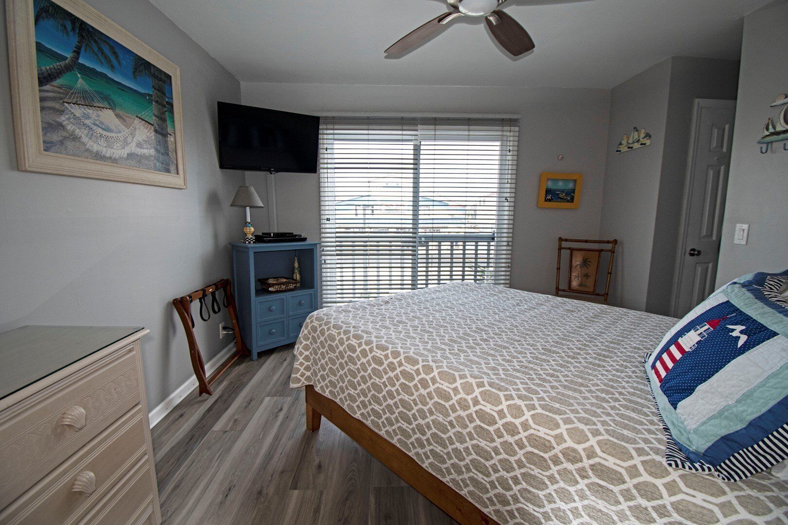 A bedroom with a bed, a dresser, a TV, and a window with blinds.