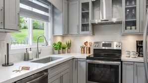 Una cocina moderna con electrodomésticos de acero inoxidable, armarios grises y un ventanal que ofrece vistas al exterior.