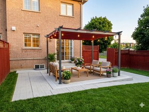 A patio with outdoor furniture, a pergola with string lights, and a brick house in the background. - Luxury 4BR Family Home, Private Fenced Yard, Near Toronto & Pearson (Mississauga)