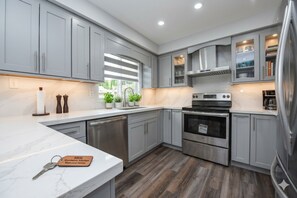 A modern kitchen with grey cabinets, stainless steel appliances, and a marble countertop. - Luxury 4BR Family Home, Private Fenced Yard, Near Toronto & Pearson (Mississauga)