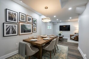 A dining area with a wooden table, chairs, and framed artwork on the wall. - Luxury 4BR Family Home, Private Fenced Yard, Near Toronto & Pearson (Mississauga)