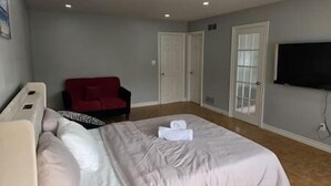 A hotel room with a bed, a red armchair, a TV, and a door. - Luxury 3BR 3BA Family Home,  Walk to Lake, Toronto (Mississauga)