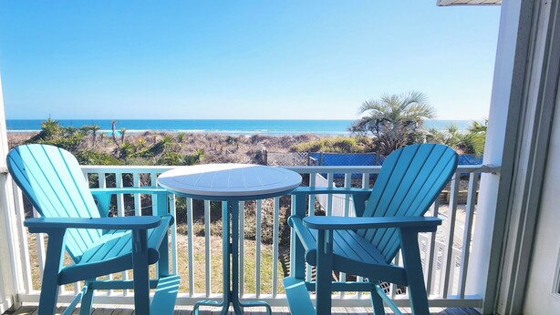 Een balkon met twee stoelen en een tafel, met uitzicht op een strand en een helder zicht op de oceaan.