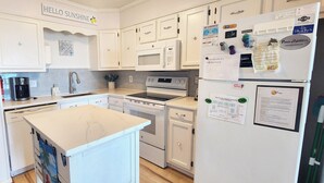 Een moderne keuken met witte kasten, een centraal eiland, een inbouwoven en een koelkast versierd met diverse magneetjes en briefjes.