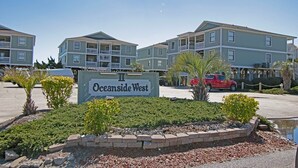 Señal de Oceanside West, un edificio residencial de varios pisos con balcones, zona de estacionamiento y áreas verdes ajardinadas.