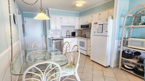 Una cocina con gabinetes blancos, una mesa de comedor de vidrio y una lámpara colgante.