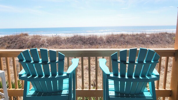 Una terraza de madera con dos sillas Adirondack turquesas mirando la playa.