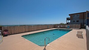 Una piscina rectangular con muelle de madera, tabloncillo de clavados y sillas de descanso.