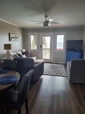 A living room with a sofa, a coffee table, and a TV. There are two doors leading to a balcony. - 2 bedroom 2 bath condo ocean view (Ocean Isle Beach)